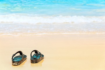 Sandal flip flop on the sand beach with blue ocean sea and sky background in summer vacation.Relaxing time on paradise.Travel,Holliday,Day off Concept. Copy space empty blank for text.