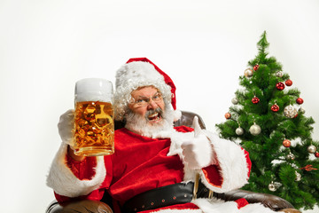 Santa Claus drinking beer near the Christmas tree, congratulating, looks drunk and happy. Caucasian male model in traditional costume. New Year 2020, gifts, holidays, winter mood. Copyspace for your