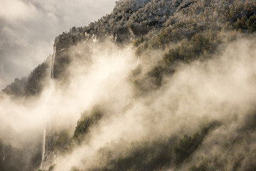 Waterfall. Trees covered with first snow and clouds.