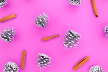 Christmas pattern. Flat lay made with many cones of silver colour and cinnamon sticks on a pink background. Top view.
