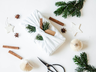 Flat lay Christmas fabric wrapped gift with paper tag, fir tree branch and cinnamon. Reusable...