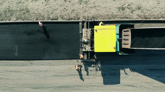 Workers are spreading bitum from the truck. Asphalt paver machine on a road construction site.