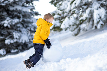 Fototapeta na wymiar Little adorable boy building snowman. Playing with snow ball. winter cold time. Smiling and laughing