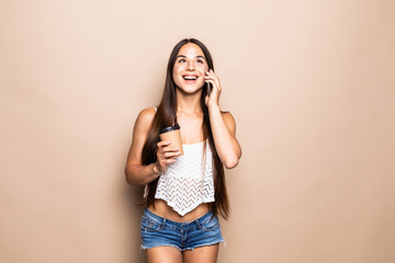 Young pretty woman with coffee cup talking on the phone on the beige background