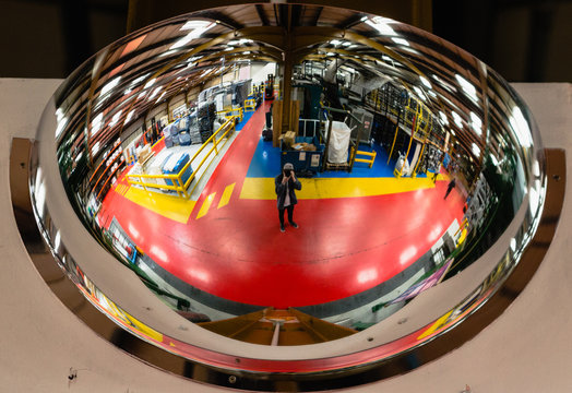 Curved circular mirror reflecting the inside of a factory for industry and production with bright reds, yellow, curved skylight reflection with photographer in reflection worker health safety mirror