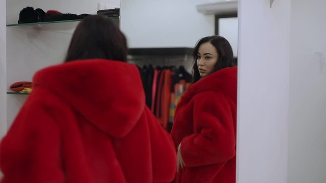 Woman buyer try on red fur coat in the boutique looking at mirror