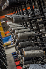 Fototapeta premium Large collection of thread and yarn in rolls stacked high on a metal grid ready to be fed down to a machine to weave them all together an industrial commercial factory create textiles materials rugs