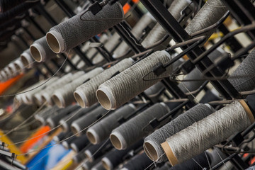 Large collection of thread and yarn in rolls stacked high on a metal grid ready to be fed down to a machine to weave them all together an industrial commercial factory create textiles materials rugs