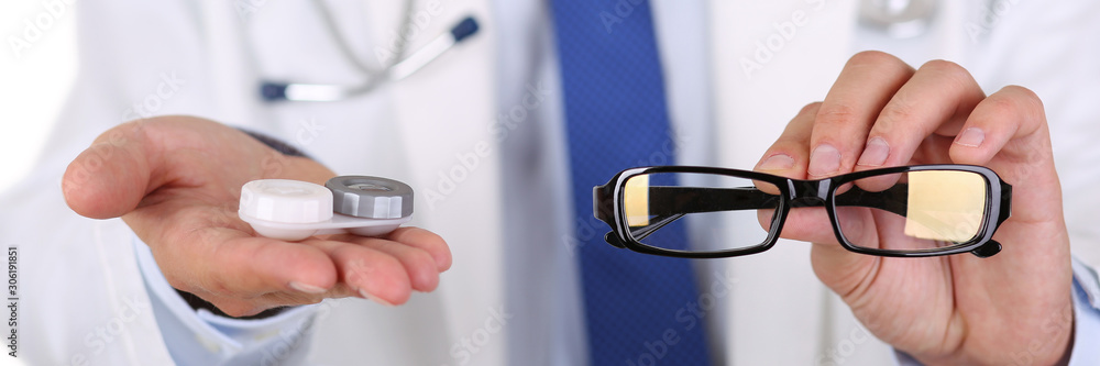 Wall mural male doctor hands giving pair of black glasses and contact lens