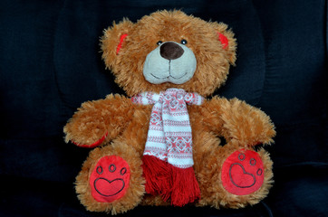 Brown teddy bear with red feet sitting in a black chair