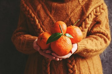 Woman in orange knitted pullover with ripe clementines in her hands. Hygge style photo