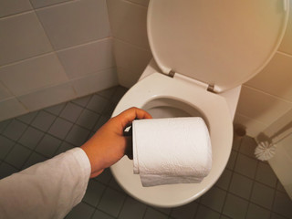A Hand holding toilet paper in the toilet