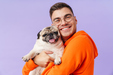 Cheery optimistic man holding hugging dog pug. - obrazy, fototapety, plakaty