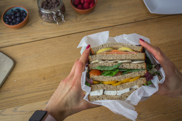 Big stacked sandwich healthy protein balanced diet chopping board hands in environmentally friendly wrapper tomato salmon pepper cheese vegetarian for body mind