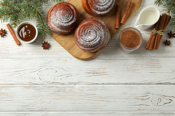Cinnamon rolls, caramel, milk and fir branches on white wooden background, top view