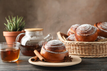 Cinnamon rolls, tea, plant and wicker basket on wooden table, space for text