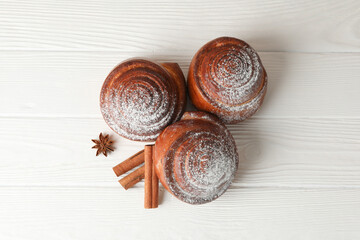 Cinnamon rolls with powdered sugar and cinnamon stacks on white wooden background, top view