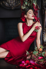 Attractive gorgeous brunette woman in red evening dress in dark luxury interior in vintage barocco style decorated flowers