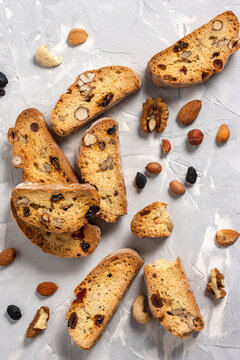 Tasty traditional Italian homemade biscotti or cantuccini cookies with hazelnuts, almonds, raisins and walnuts on a light gray background.