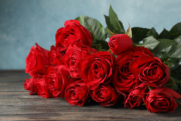 Bouquet red roses on wooden table against blue background, close up