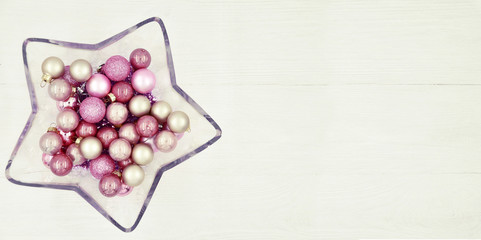 Star shaped glass vase with Christmas balls on a wooden white background.
