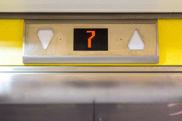Number 7 on an elevator shaft going up or down yellow above metal electronic doors in office dirty grimy for transport using technology in factory car park