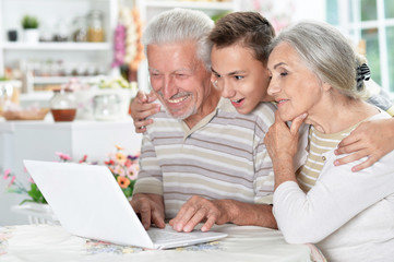 Fototapeta na wymiar Portrait of happy senior couple with grandson using laptop at home