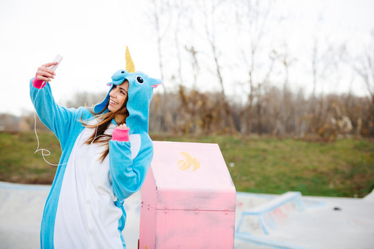 Beautiful Young Woman Wearing Turquoise Unicorn Onesie In Urban Environment