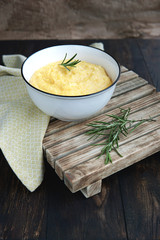   Creamy corn traditional polenta or mamaliga with butter. Served in white shallow dish on rustic wooden table with rosemary. Country style. Selective focus, copy space. Healthy organic food concept.