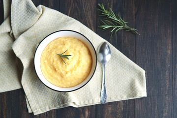  Creamy corn traditional polenta or mamaliga with butter. Served in white shallow dish on rustic wooden table with rosemary. Country style. Selective focus, copy space, top view. Healthy  food concept