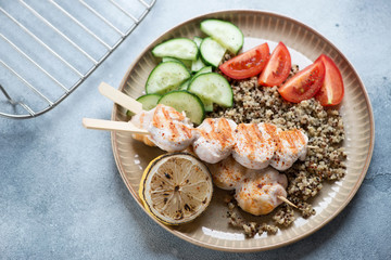 Beige plate with fried chicken fillet on skewers, quinoa and fresh vegetables, studio shot over light-blue stone surface