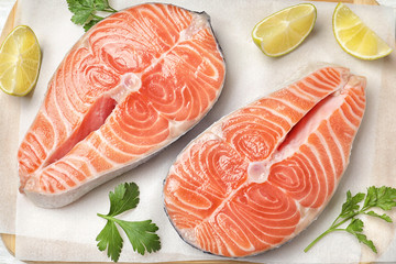 Fresh raw salmon with parsley and lime on parchment, flat lay. Fish delicacy