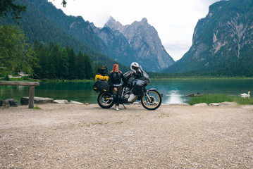Fototapeta na wymiar Girl motobiker in the center of the composition stands with tourштп motorcycle. Extreme travel vacation, motorcyclist adventure lifestyle. Toblacher See, (Italian: Lago di Dobbiaco) Italy. copy space