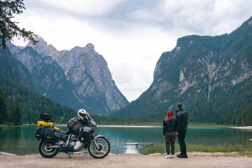 Motorcyclists couple look at distance with touring notorcycle. Lake and Alpine mountains on...