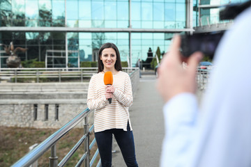 Young male journalist and video operator working on city street