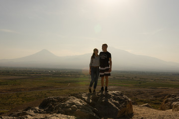 A girl and a guy travel together in Armenia, Yerevan. At sunset, they jump silhouettes against the backdrop of Mount Ararat.