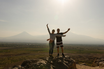 A girl and a guy travel together in Armenia, Yerevan. At sunset, they jump silhouettes against the backdrop of Mount Ararat.