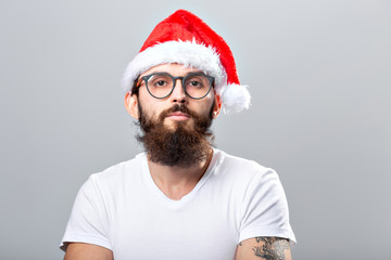 Holidays and people concept - Portrait of a handsome brutal man in Christmas hat. Over grey background.