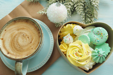 A cup of coffee with foam, a heart-shaped box with meringues of different colors, a Christmas ball and a fir branch....
