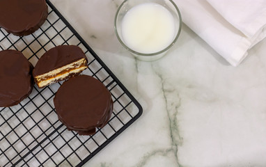 Top view of Homemade alfajores de chocolate, typical from Argentina, over cooling rack with milk over marbled background with copy space