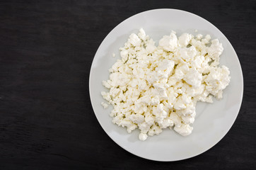 white cottage cheese in a white plate on a black table. Place for text. View from above.