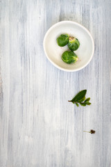 Brussels sprouts in bowl and green stem with leaves on light wooden background. Place for an inscription