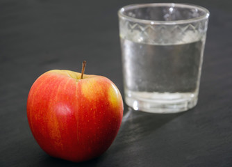 red apple and a glass of water on a black background.