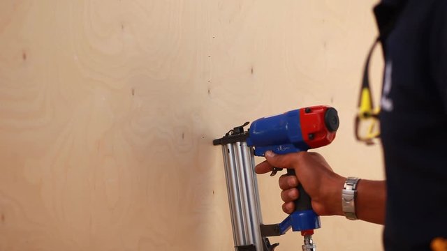 wooden carpenter using air compressor nail gun.The worker makes finishing works of walls with white wooden board