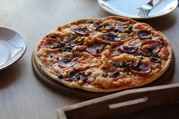 Tasty hot pizza on a wooden plate. Cutlery. Food in cafe
