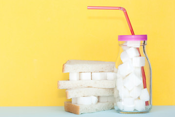 Glass full of sugar and sandwich with sugar cubes. Unhealthy food cocept.