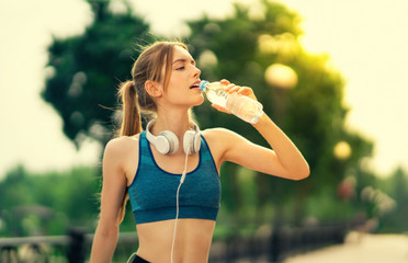 Lovely girl in sportswear drinking water, during morning jogging or workout, outdoors. Fitness, sport, crossfit and exercising concept. Girl holding bottle of water, at park.