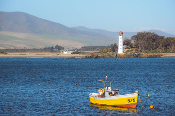 Yellow fishing boat in the sea with a lighthouse in the background