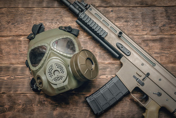 Airsoft rifle and gas mask on brown wooden table background.