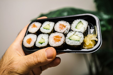 Close-up macro shot of man hand holding fresh delicious sushi maki black plastic box with delicious bio organic ingredients